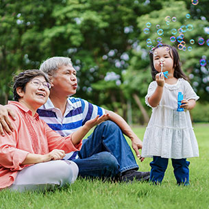 A couple watching their grandchild blowing bubbles. Links to Gifts That Protect Your Assets